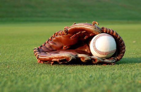 A baseball glove lays on the grass of a baseball field with a baseball in its pocket.